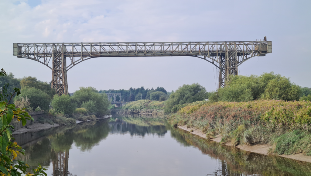 A picture of the transporter bridge spanning the river Mersey in Warrington. It is a girder structure of  two upright towers with a span across.